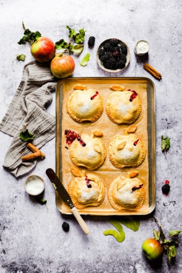 overhead shot of baked apple and blackberry hand pies on a baking tray