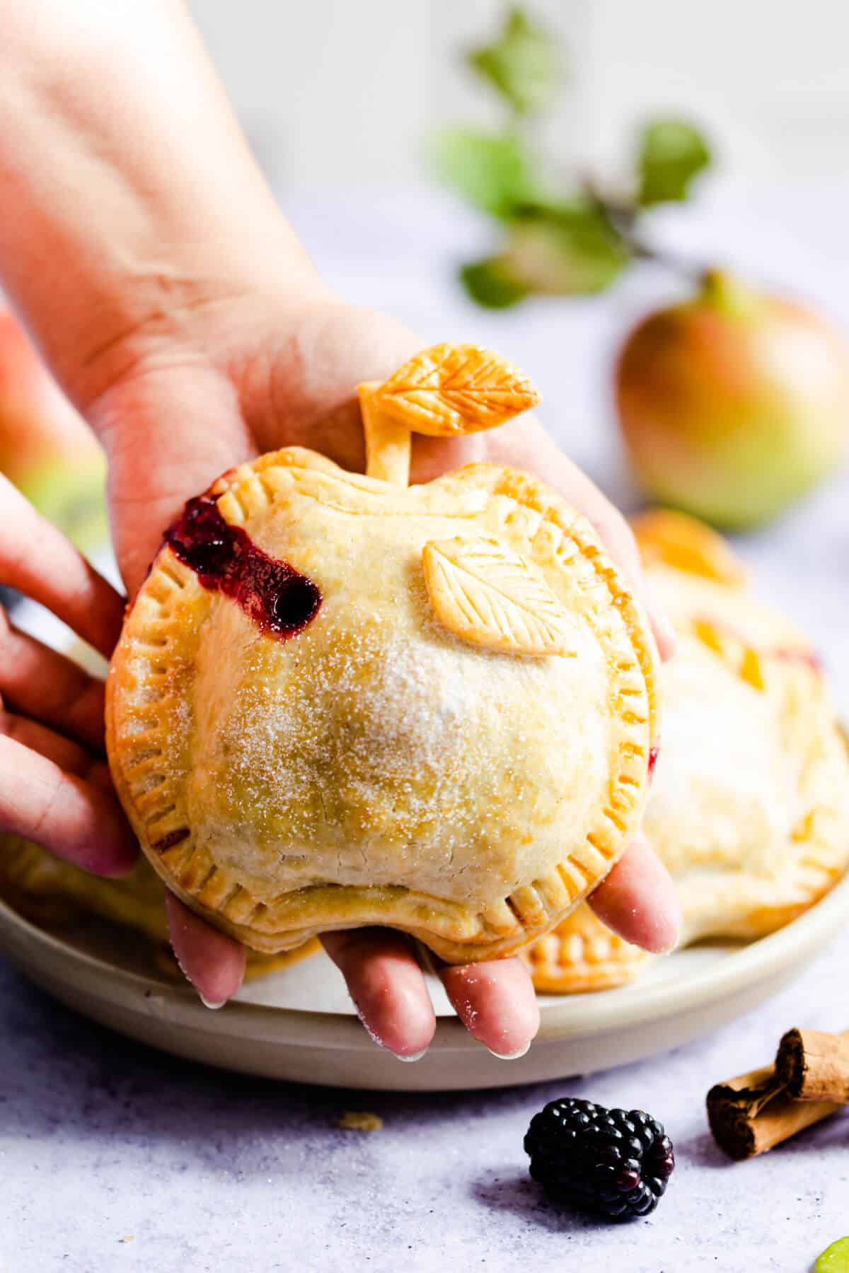 side close up of a person holding a pie shaped like an apple in palm of their hand