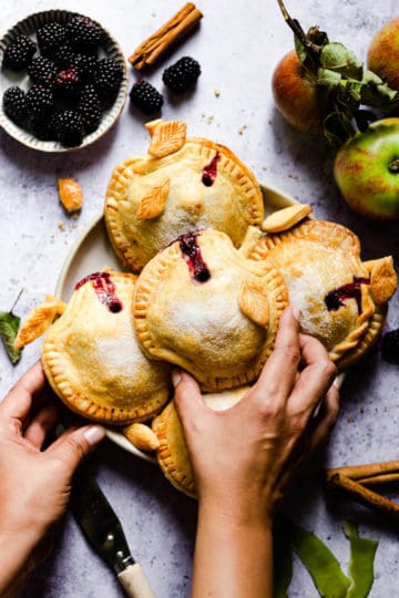 overhead shot of a person reaching to a plate with spiced apple and blackberry hand pies