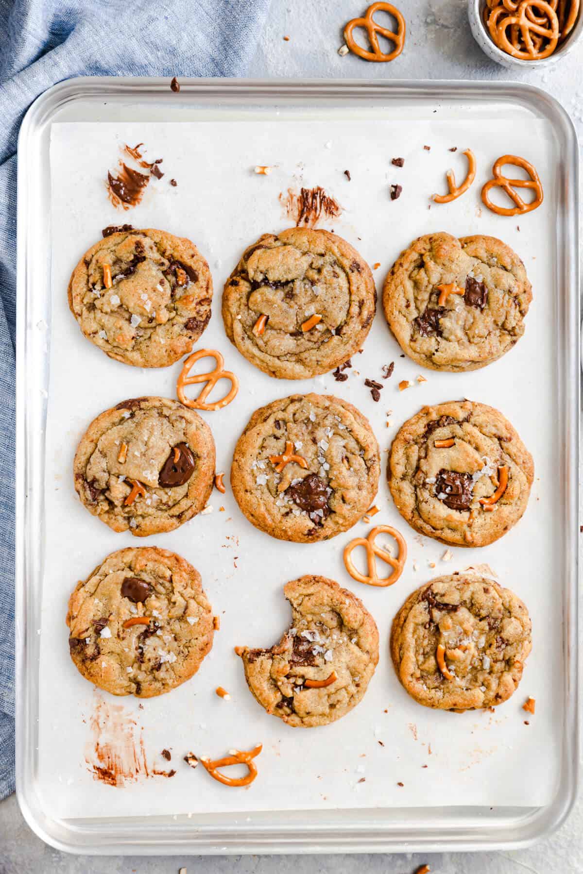 overhead shot at a baking tray with 9 cookies topped with pretzels and one cookie missing a bite