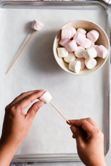 overhead shot of a person poking a bamboo skewer through a marshmallow