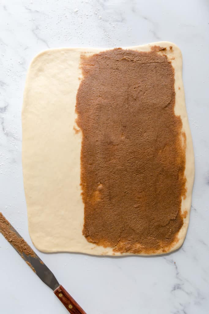 overhead shot of a dough rolled into rectangle with cinnamon butter spread on ⅔ of it