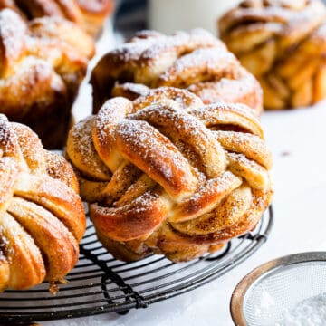 twisted cinnamon bun dusted with icing sugar on a round wire rack.