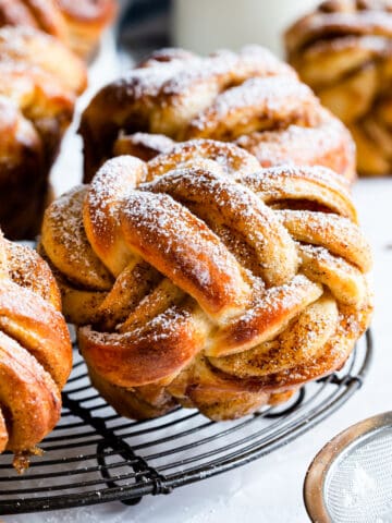 twisted cinnamon bun dusted with icing sugar on a round wire rack.