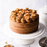 coffee and walnut cake topped with buttercream and nuts on a white cake stand.
