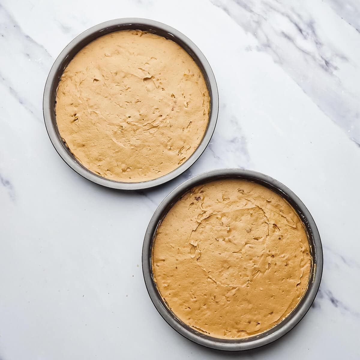 two round baking tins with cake batter inside.