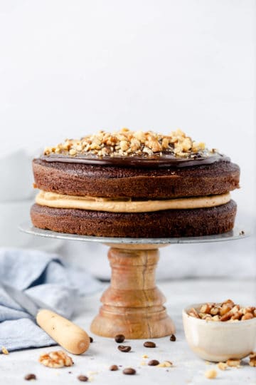 straight ahead shot of a coffee cake on a cake stand topped with ganache and chopped walnuts