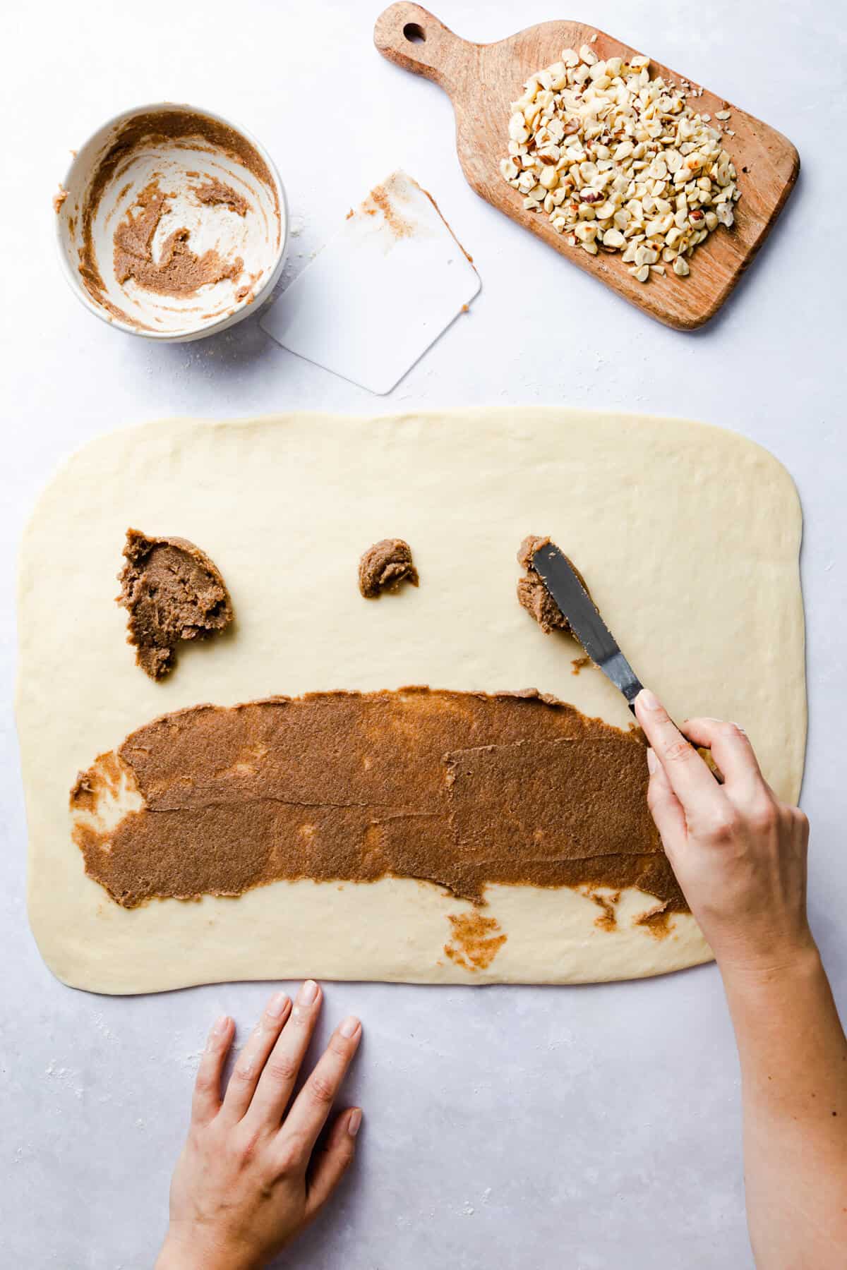 top view of a person spreading cinnamon butter on the surface of dough rectangle