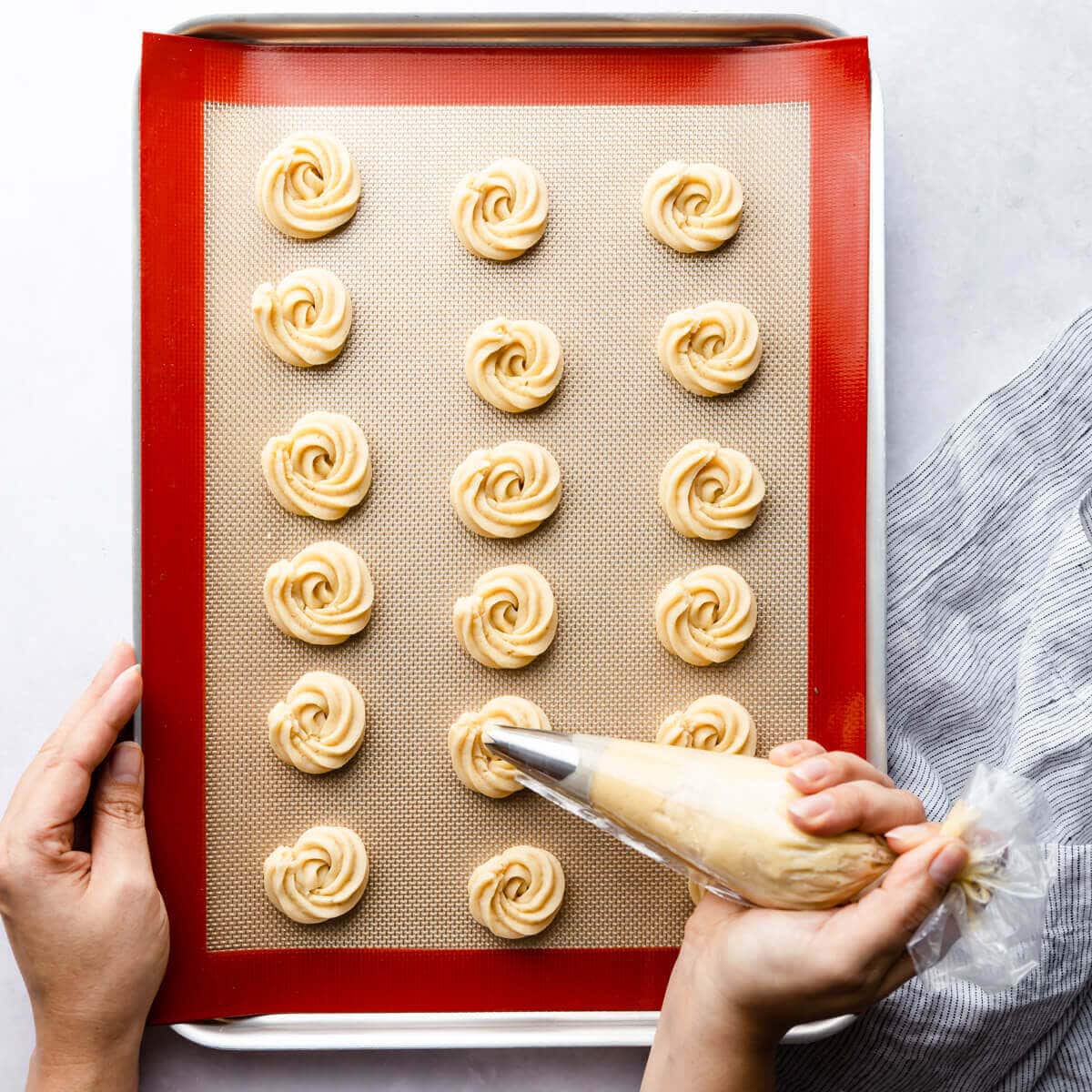 a person piping the cookies into a baking sheet with silicone mat.