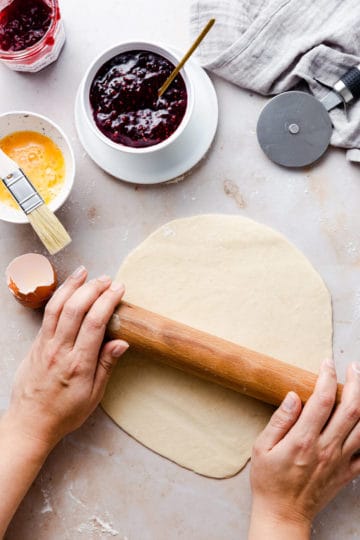 top view of a person rolling the dough into circle with wooden rolling pin