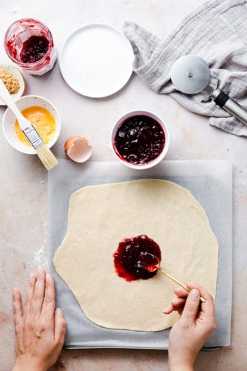 overhead shot of a person spreading some raspberry jam on top of rolled dough