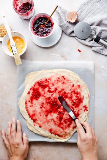 overhead shot of a person spreading some jam on a layer of rolled dough