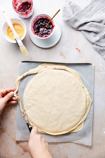 overhead shot of a person using pizza cutter to trim the dough into circular shape