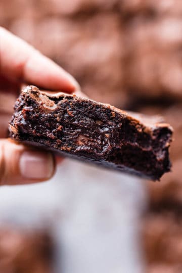 super close up of a person holding a slice of brownie showing it's gooey texture