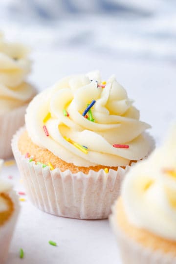side close up of a one bowl vanilla cupcake with buttercream and coloured sprinkles on top