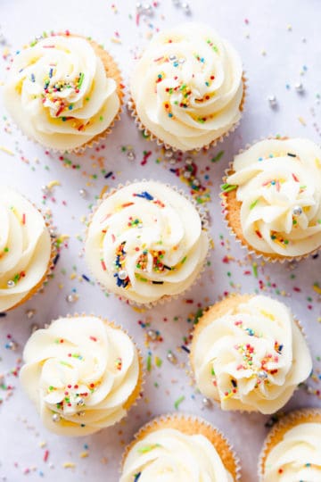 overhead shot of vanilla cupcakes with buttercream and colourful sprinkles