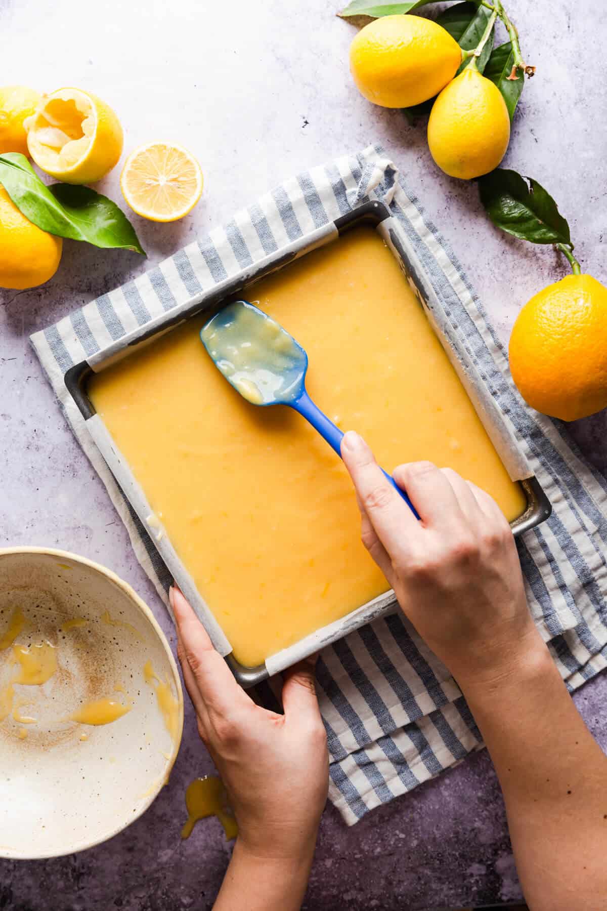 overhead shot of a person smoothing the top of lemon curd slices with spatula
