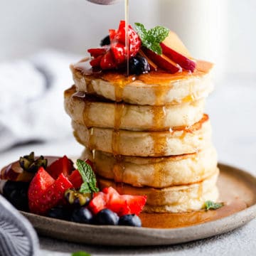 straight ahead angle photo of a stack of fluffy pancakes drizzled with maple syrup