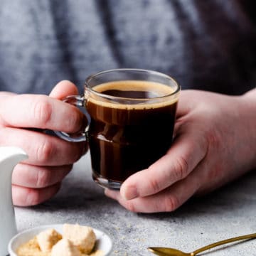 side close up of a person holding a small cup of coffee