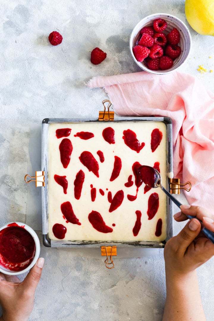 overhead view of a person adding raspberry sauce on top of cheesecake batter