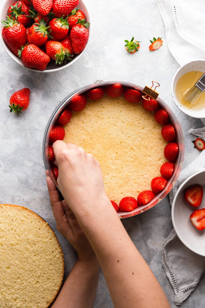 overhead shot of a person fitting fresh strawberries inside of the baking tin