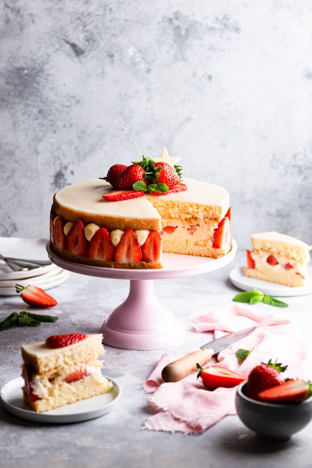 side view of strawberry cake on pink cake stand with couple of slices cut out