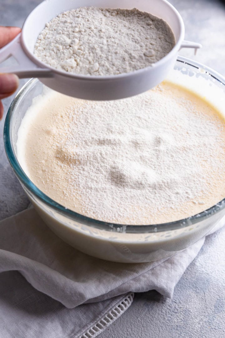 side view of a cake batter in a bowl with flour being sieved on top