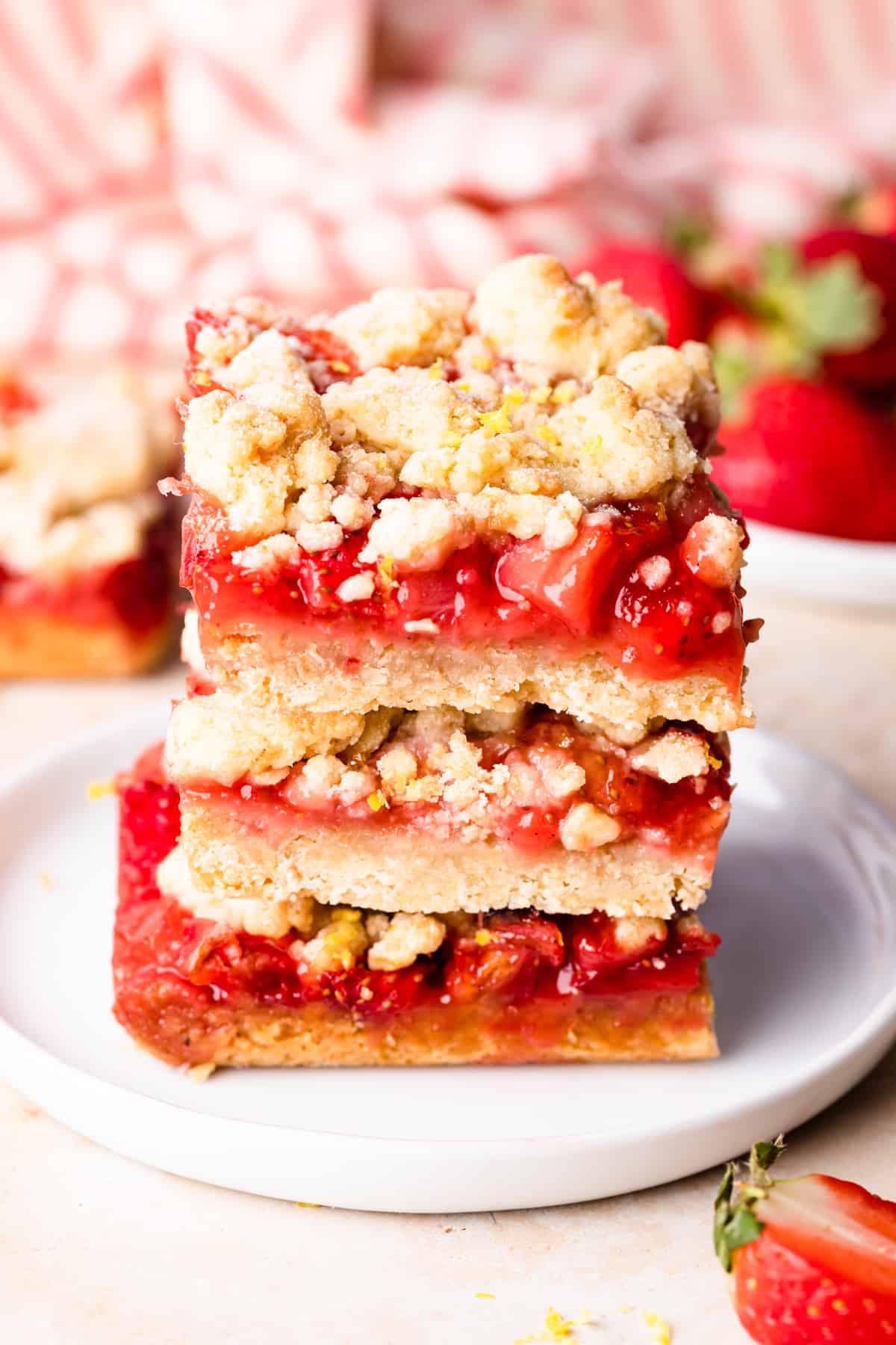 three strawberry crumble bars stacked on top of each other on a small white plate.