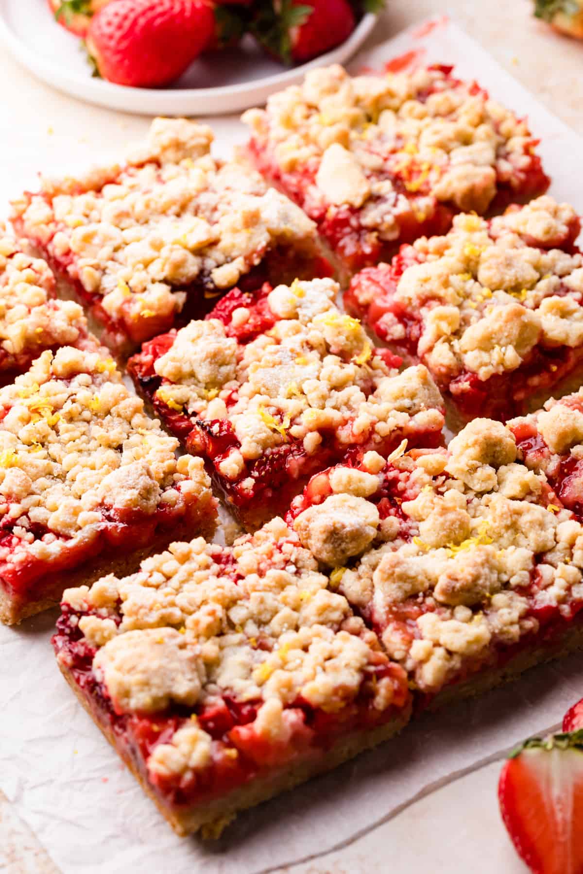 crumble bars with strawberries and streusel topping resting on a slice of baking paper.