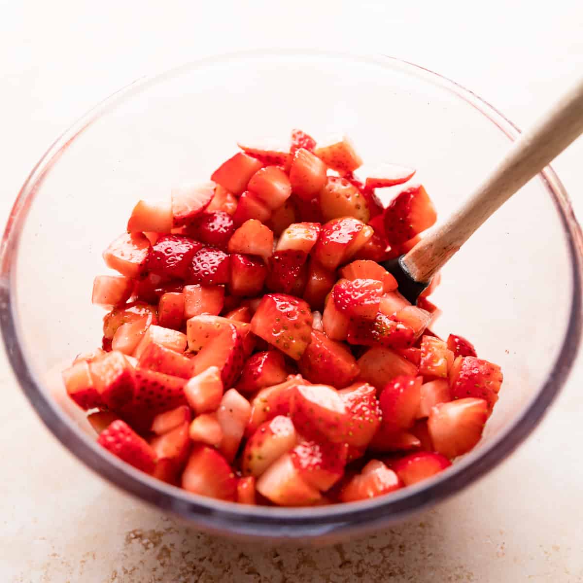 glass bowl with chopped strawberries and small spatula inside of the bowl.
