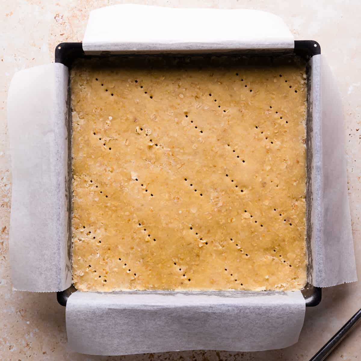 square baking tin lined with baking parchment and with crumble dough pressed into the base of it and pricked with fork.