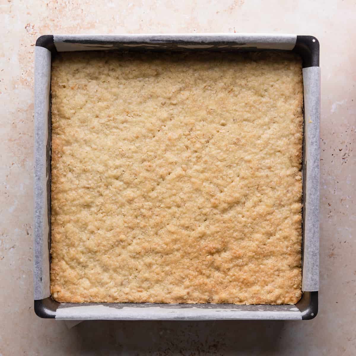 square baking tin lined with paper and with baked crumble base inside.