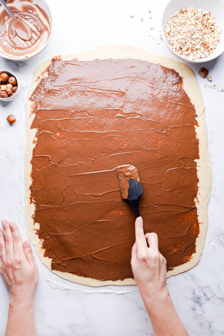 top view of a person spreading nutella on top of rolled dough