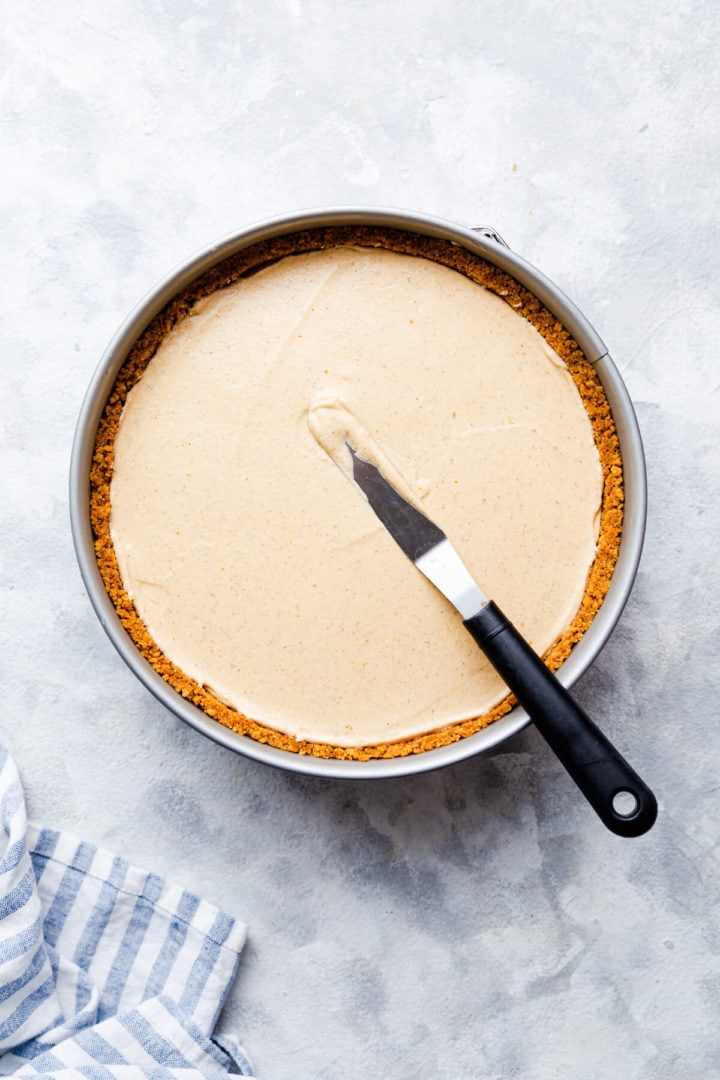 top view of a round baking tin with pumpkin cheesecake inside and small offset spatula on tiop