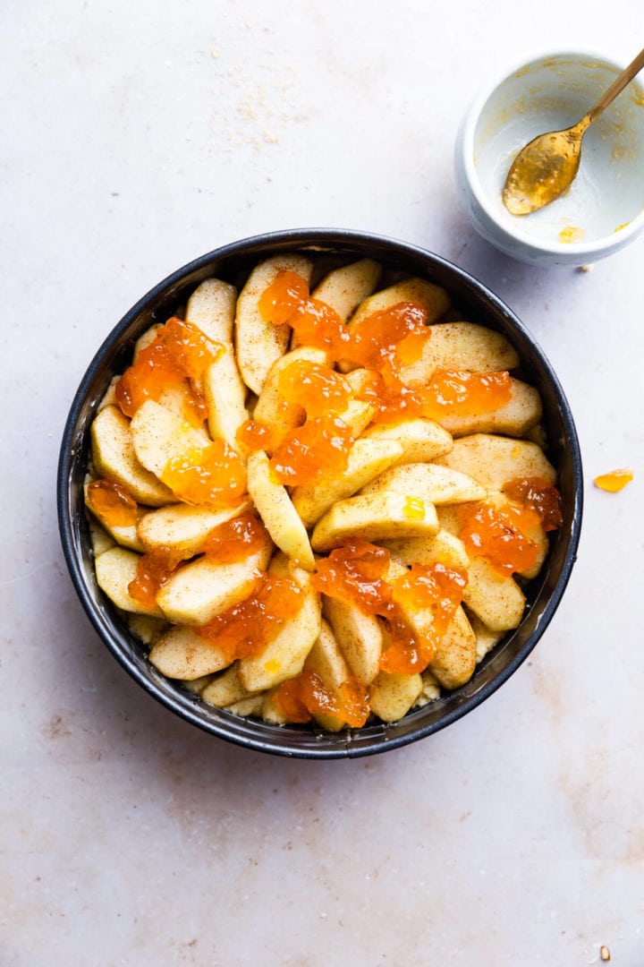 overhead shot of round baking tin with sliced apples and jam on top