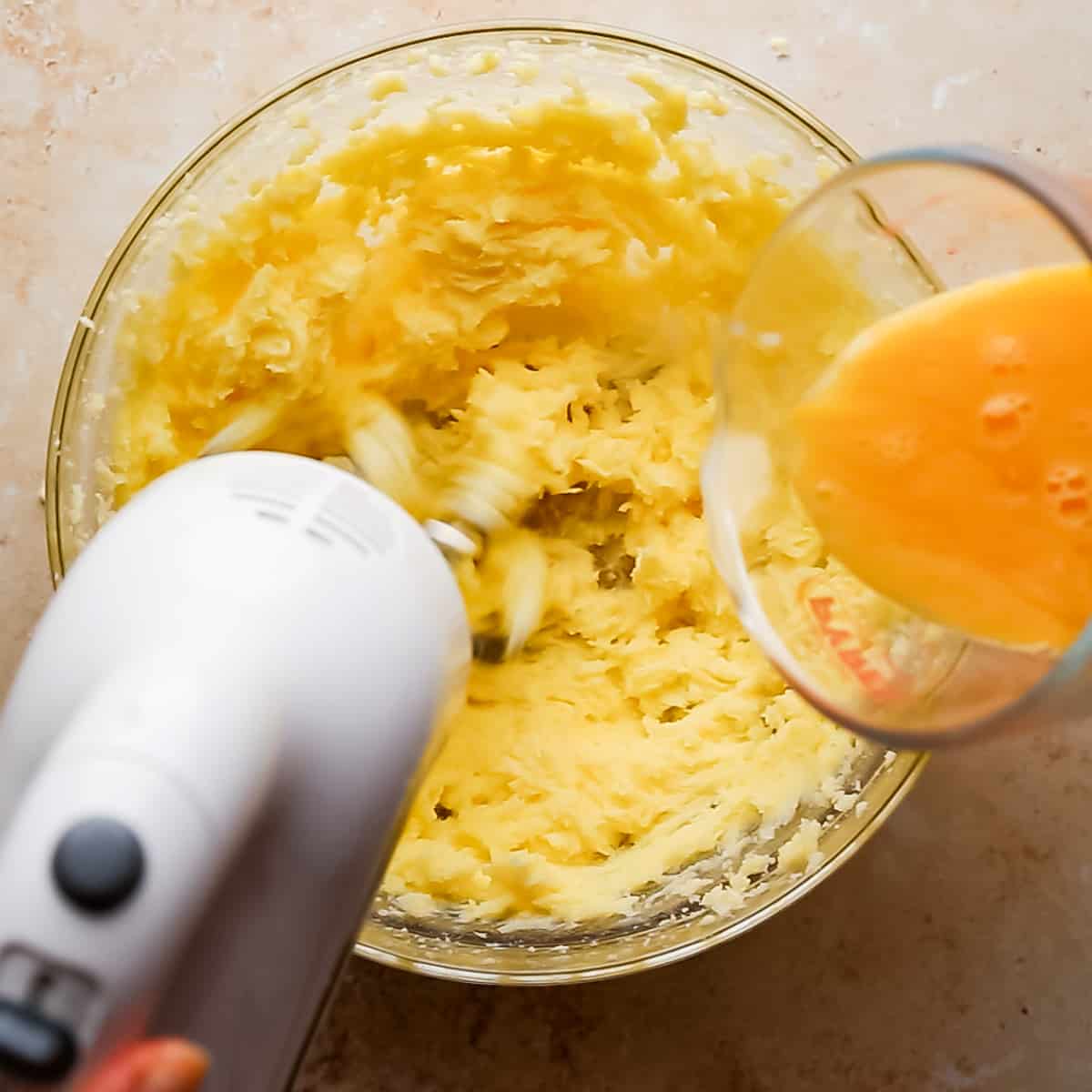 bowl with creamed butter and sugar and eggs being poured into it while mixing with electric mixer.