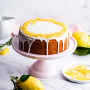 zesty lemon cake with icing and lemon peel decoration on a pink cake stand.