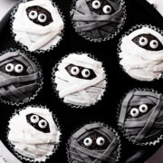 chocolate cupcakes decorated with black and white icing and sugar eyes on a black background.