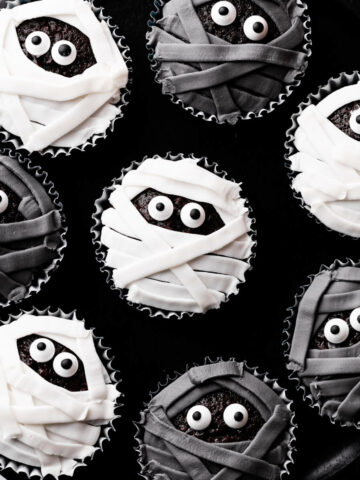 chocolate cupcakes decorated with black and white icing and sugar eyes on a black background.
