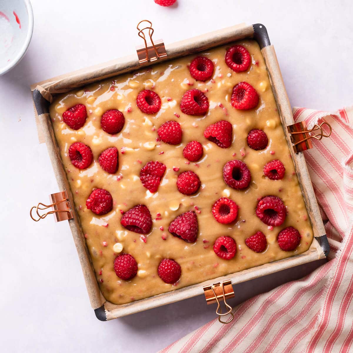 baking tin with blondie batter and fresh raspberries on top of it.