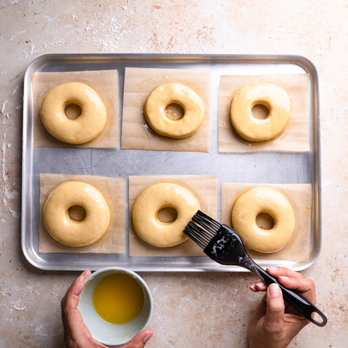 unbaked doughnuts being brushed with melted butter.