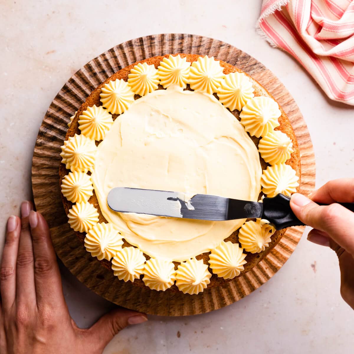 custard buttercream being spread with an offset spatula on top of the sponge cake.