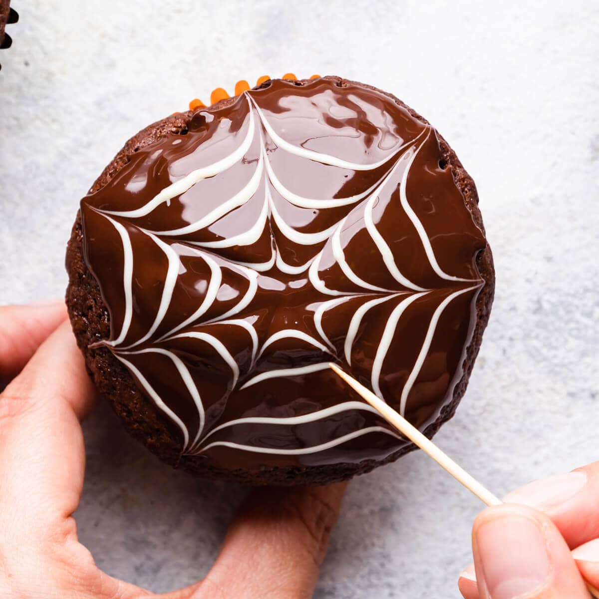 a chocolate web decoration in the making on top of the chocolate muffin.