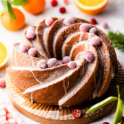 bundt cake on wooden cake board topped with cranberries covered in sugar.