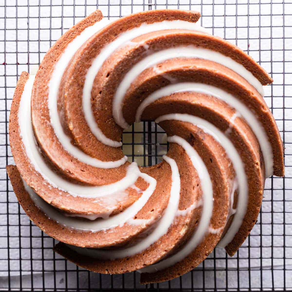 orange cranberry bundt cake drizzled with glaze on a cooling rack.