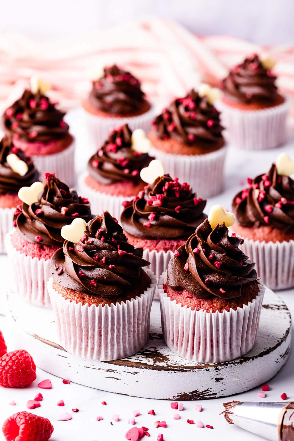 chocolate and raspberry cupcakes on a small white wooden board.