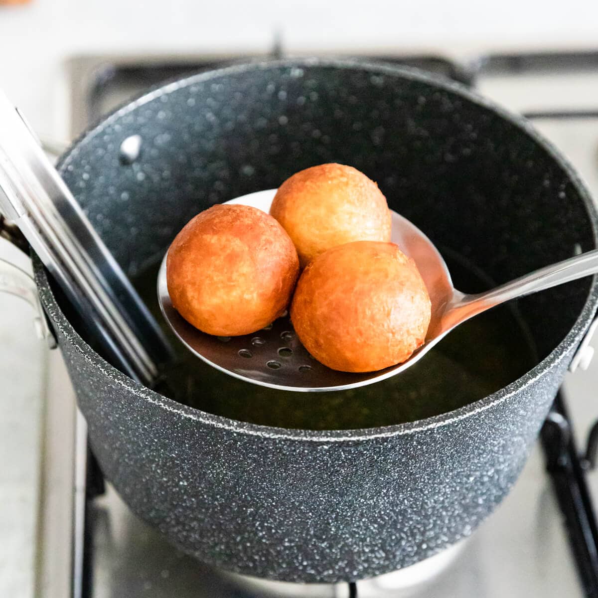 donut holes being taken out of the hot oil with slotted spoon.