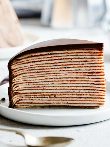a slice of chocolate crepe cake with ganache on a white plate.