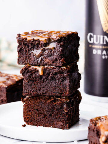 stack of 3 chocolate Guinness brownies on a white plate with can of Guinness in a background.