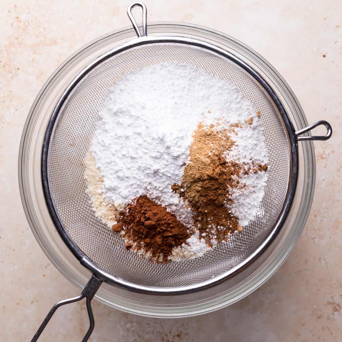 fine metal sieve filled with almond flour, powdered sugar, spices and cocoa on top of mixing bowl.